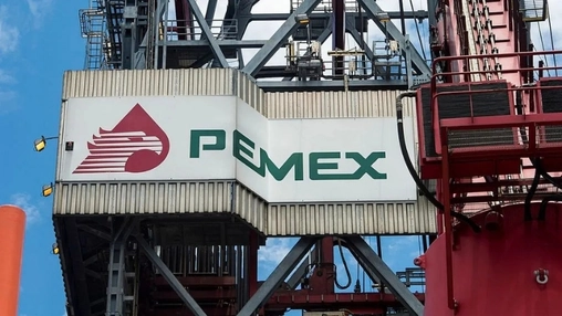Pemex logo and wordmark on a white panel attached to red offshore platform metalwork against a blue sky