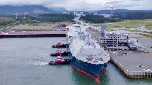 Aerial view of a large LNG tanker docked at a terminal with three tugboats positioned alongside the hull